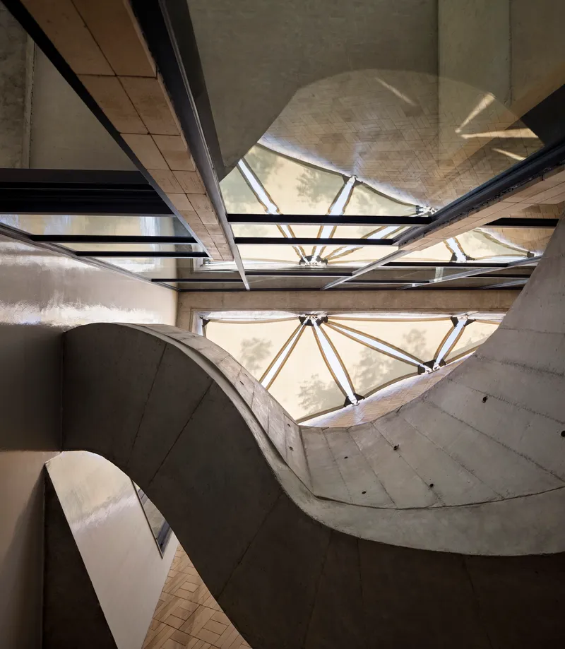 View looking up at the concrete stairwell with triangular skylights and steel bracing overhead