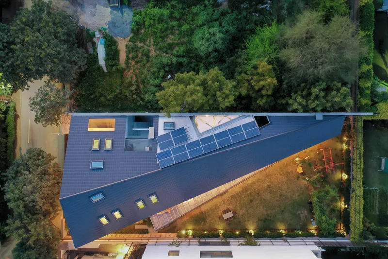 Aerial view of the angular roof with solar panels and skylights surrounded by dense vegetation at dusk