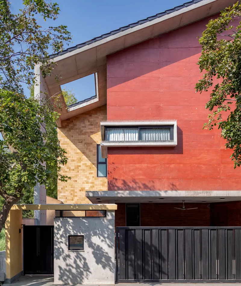 Red sandstone and ochre brick facade with horizontal window band and tree shadows on the entry wall