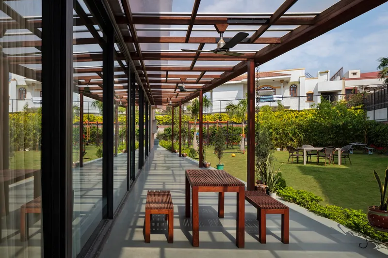 Covered terrace with timber pergola beams, slatted dining furniture, and view to planted lawn beyond