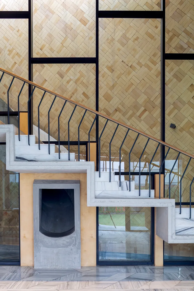Black metal staircase with curved railing rising past herringbone bamboo wall panels and fireplace surround