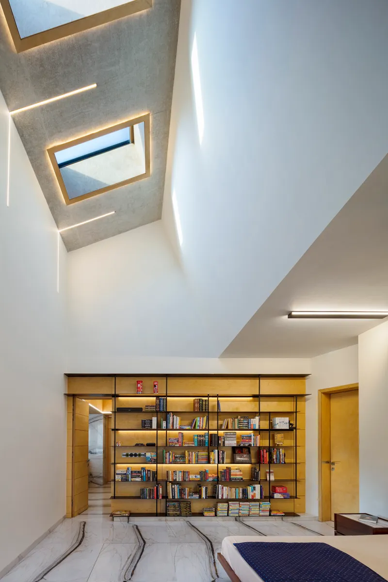 Double-height library space with skylights, timber bookshelves, and recessed cove lighting along white walls