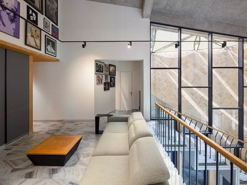 Double-height living space with steel-framed glazing overlooking a diagonal brick facade and exposed concrete ceiling