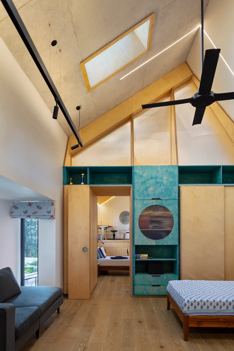Vaulted bedroom interior with plywood storage unit featuring circular porthole openings and integrated green shelving