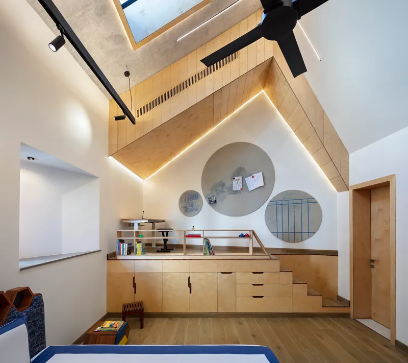 Plywood loft platform with circular wall niches and built-in storage cabinets under a vaulted ceiling