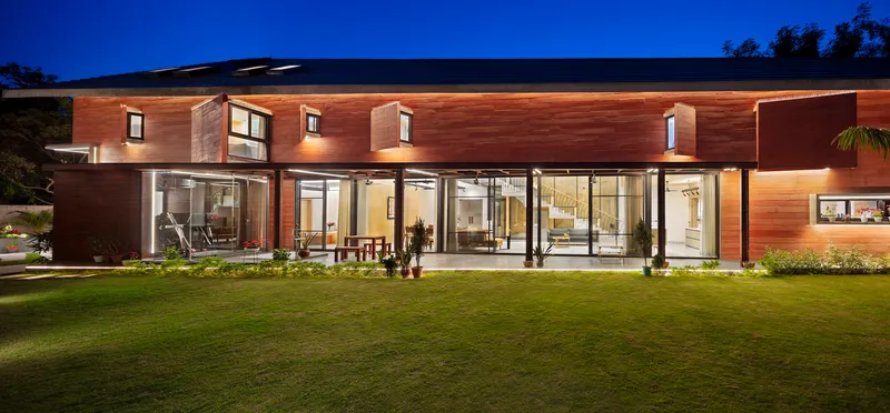 Rear elevation with horizontal timber cladding and continuous glazed openings illuminated at twilight above a lawn