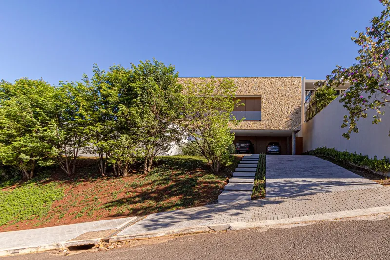 Street view of the stone-clad facade with sloped lawn and concrete steps under clear blue sky