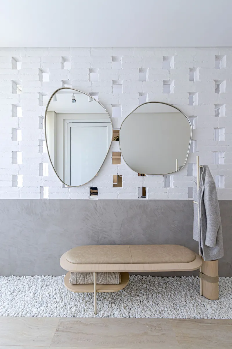 Bathroom vanity with two oval mirrors on white geometric tile above a timber bench