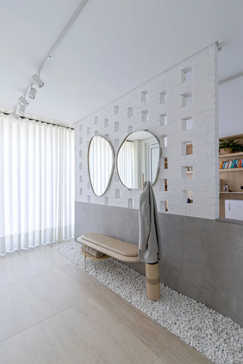 Interior wall with textured white tile and three oval mirrors above a concrete ledge with white pebbles