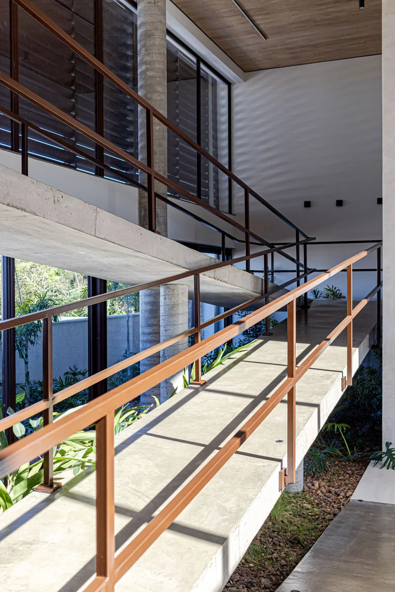 Cantilevered concrete walkway with timber handrails spanning a sunlit interior courtyard with planted beds below
