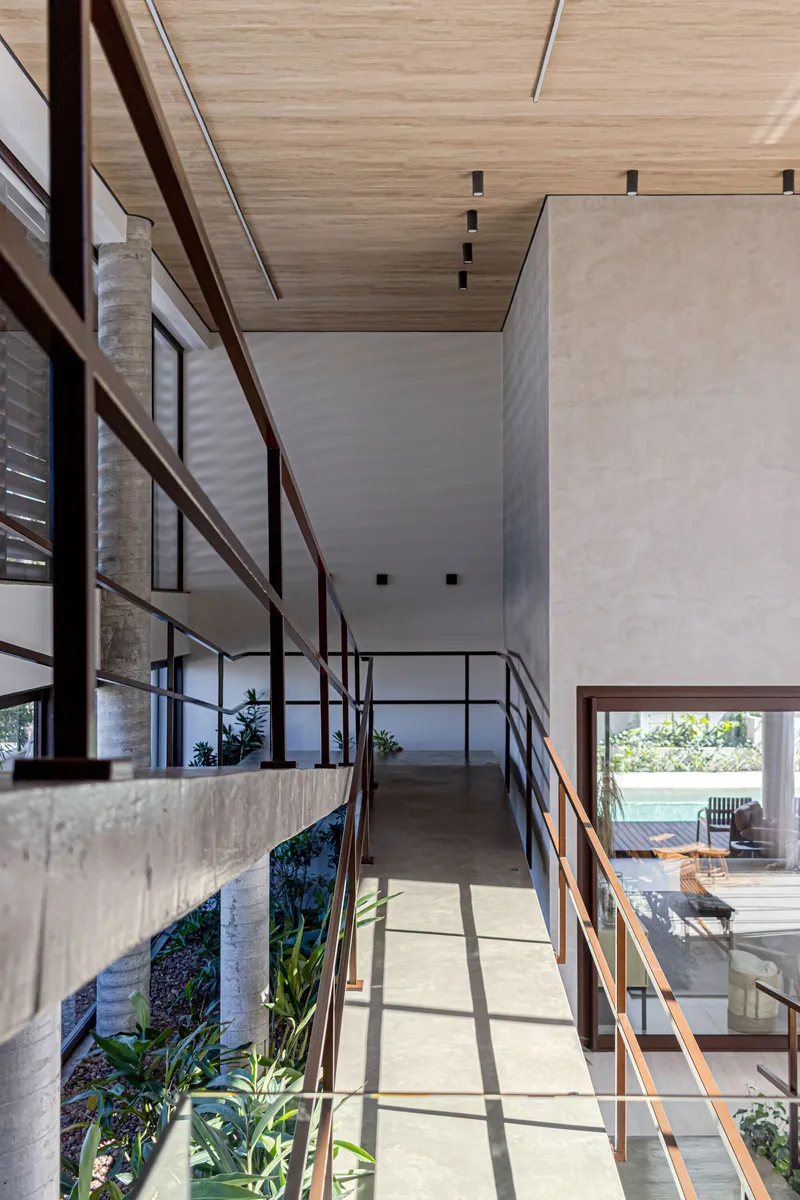 Upper-level walkway with concrete beam, steel railings and timber-clad ceiling casting sharp shadows