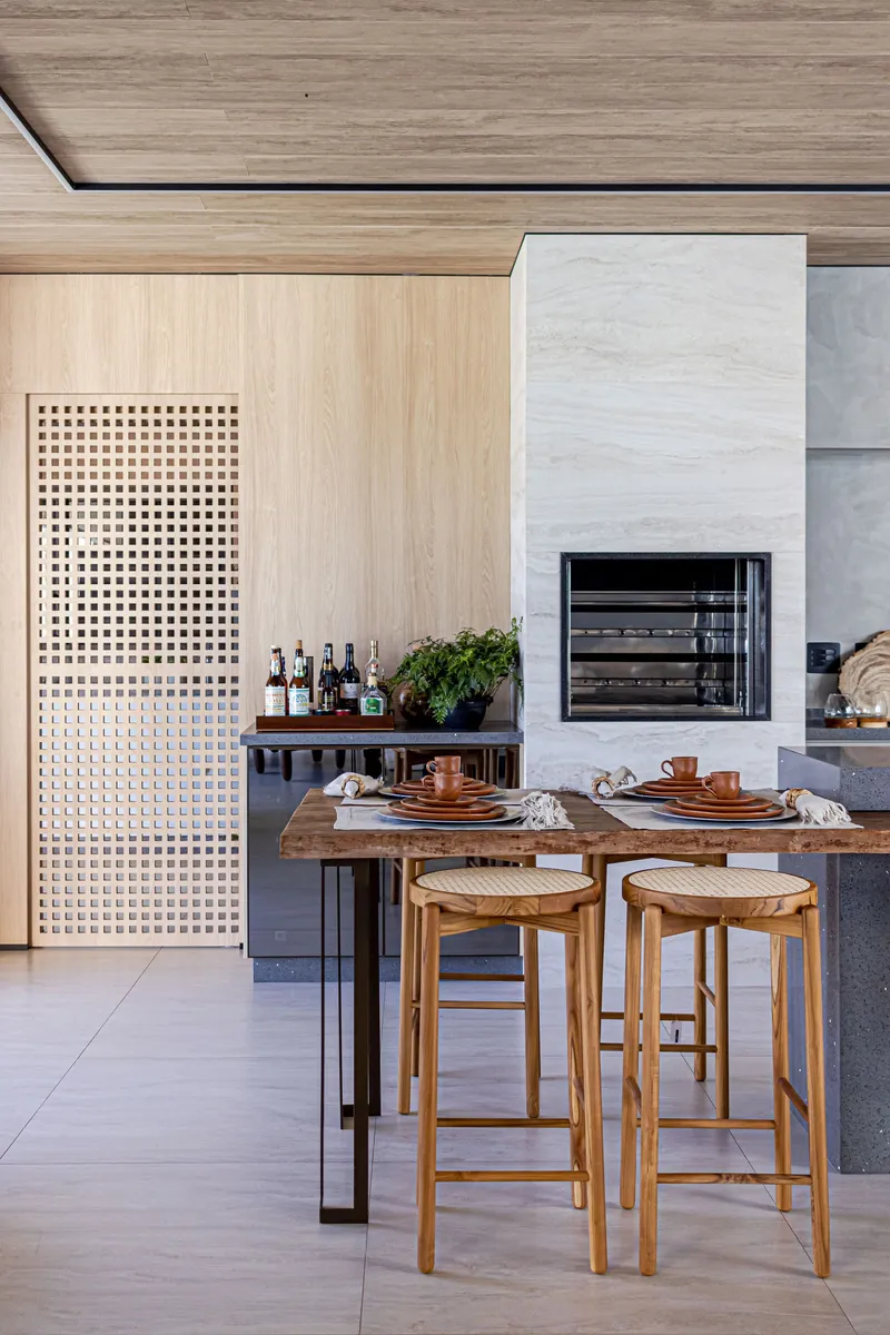 Outdoor kitchen with perforated timber screen, pale stone fireplace and timber breakfast bar with stools