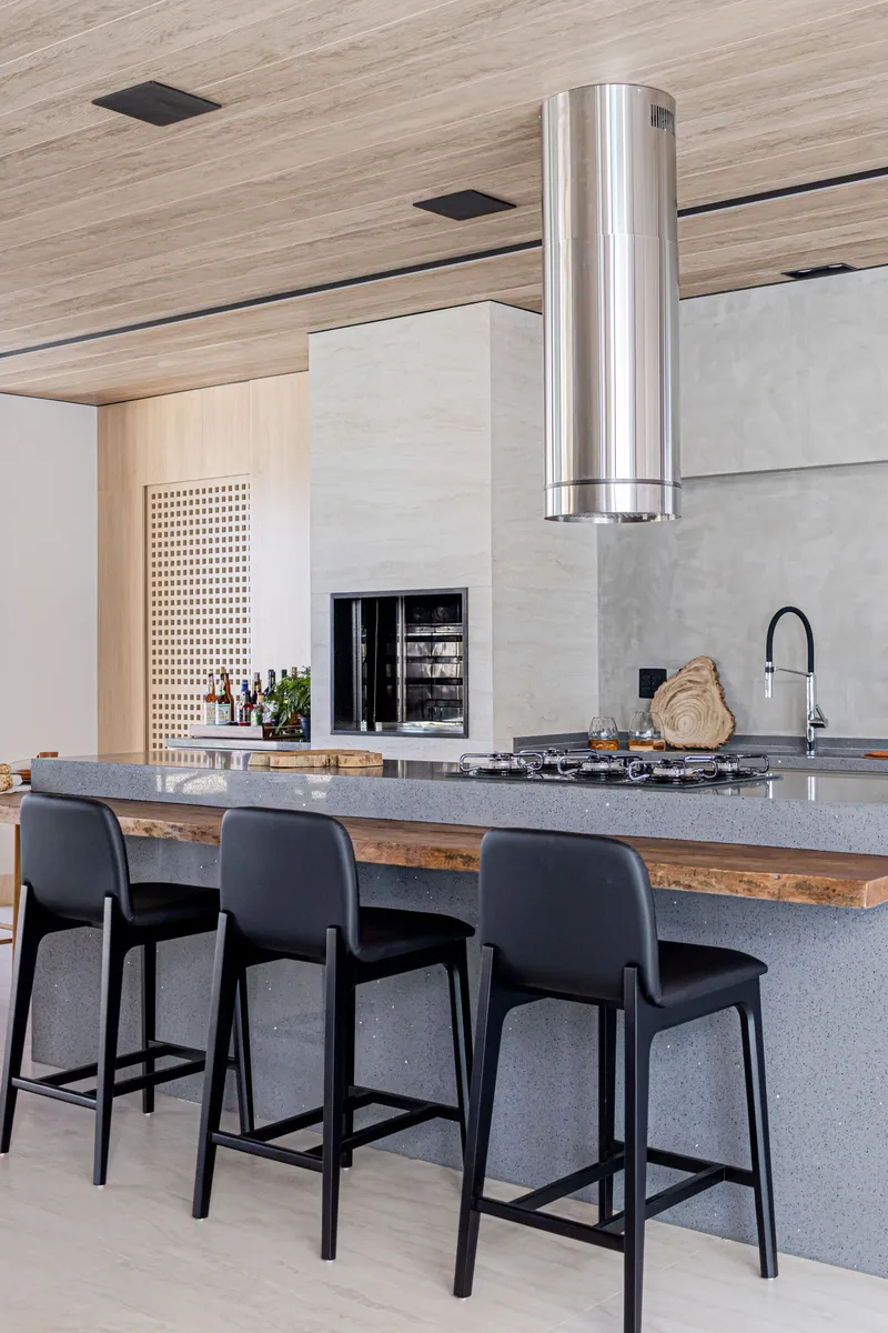 Kitchen island with polished stone countertop, cylindrical steel hood and reclaimed timber edging under timber ceiling