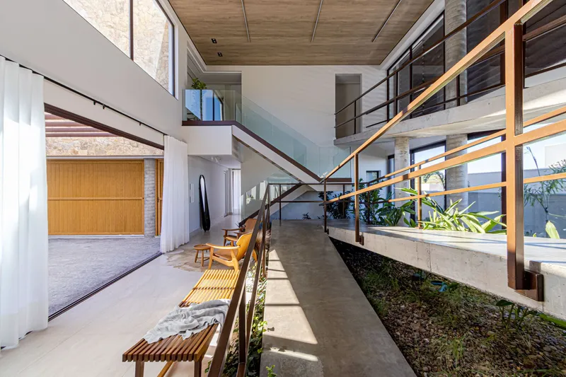 Interior bridge walkway above planted courtyard with horizontal metal railings and timber louvers