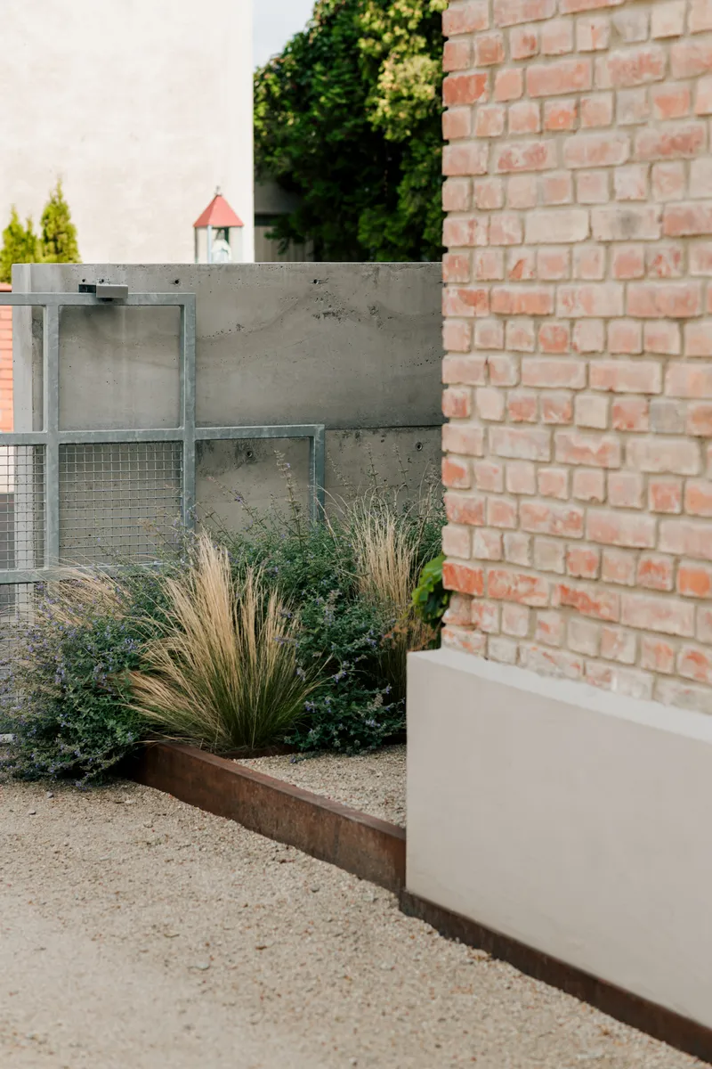 Garden view showing concrete wall and brick facade with planted grasses in corten-edged bed