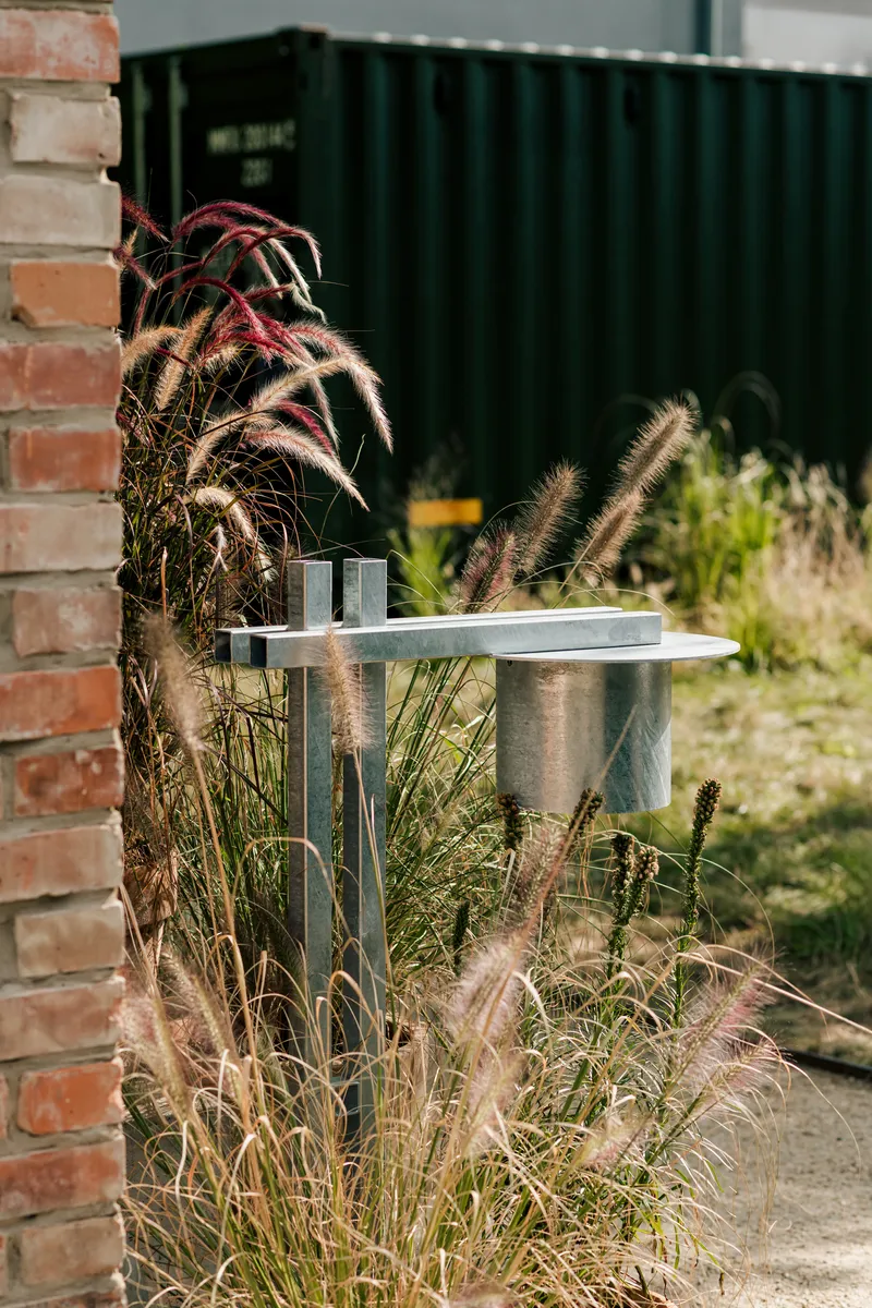 Outdoor tap on galvanized post surrounded by ornamental grasses beside brick wall