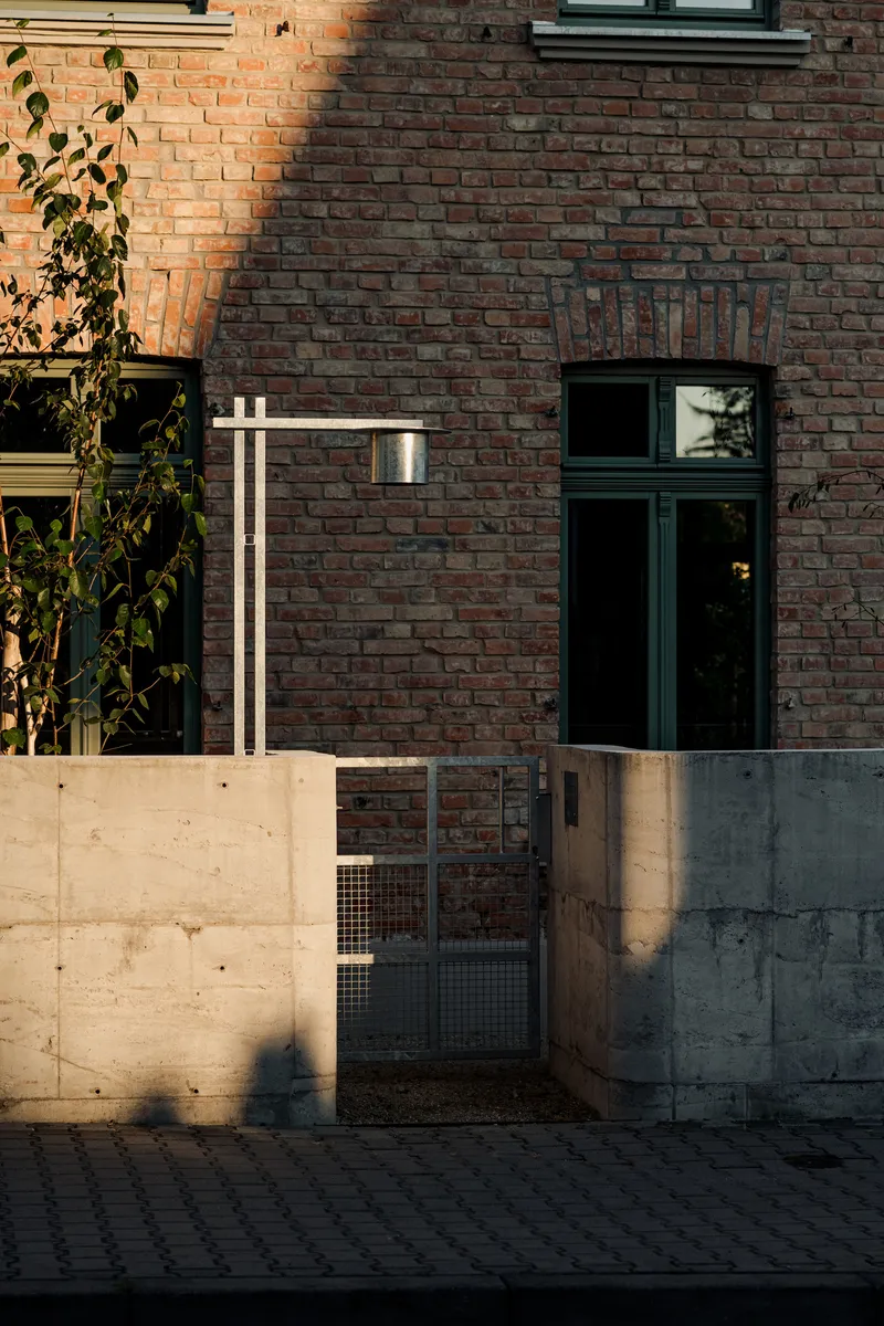 Red brick facade with concrete base wall and metal mesh gate in low afternoon sunlight