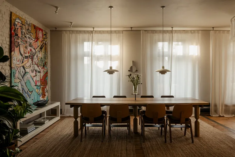 Dining room with wooden table, pendant lights, and sheer curtains filtering afternoon sunlight