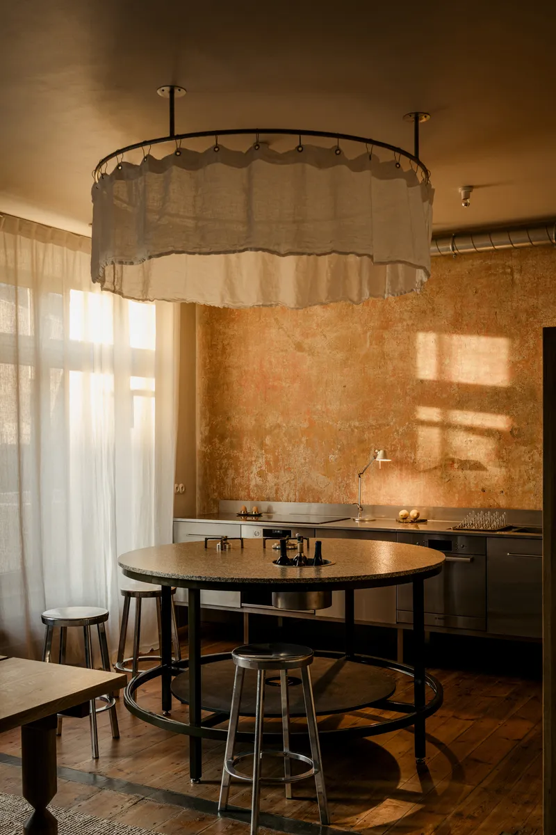 Kitchen with circular fabric canopy light fixture above round table and textured plaster wall behind