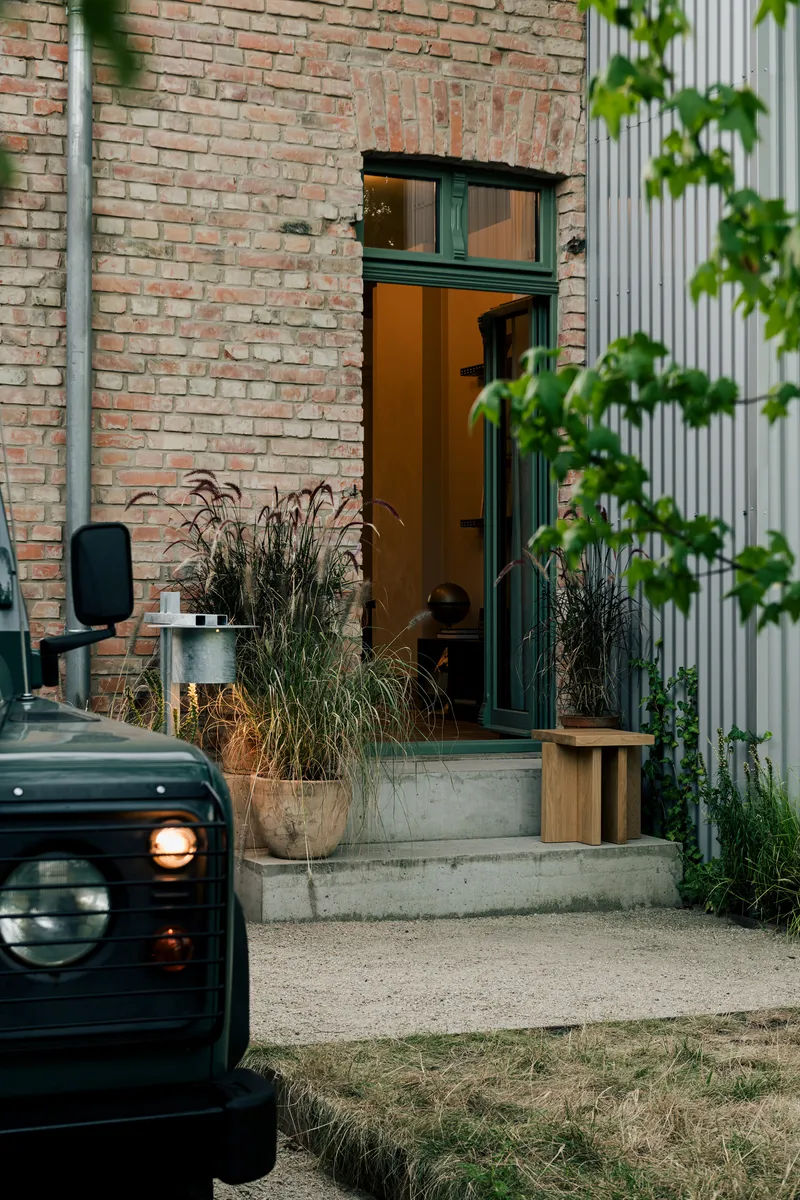 Entry door in weathered brick wall with potted grasses and parked vehicle in foreground