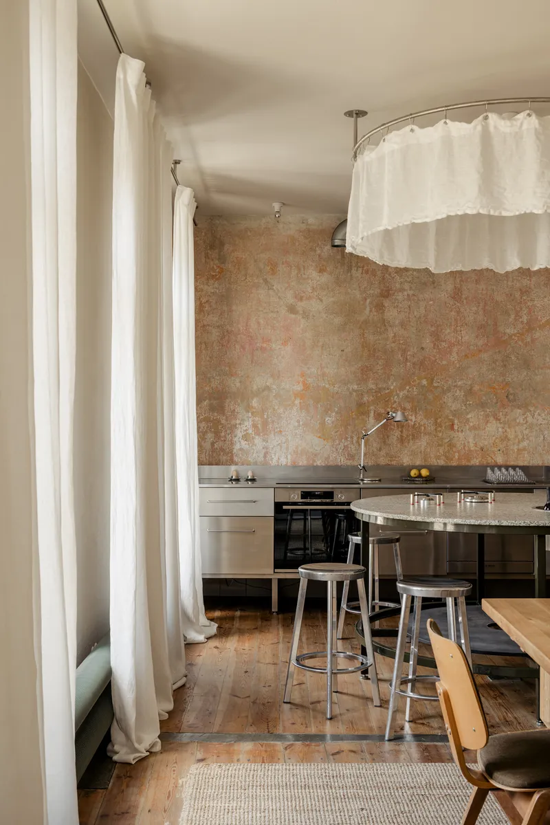 Kitchen with weathered plaster wall, white fabric curtain dividers and reclaimed timber floorboards