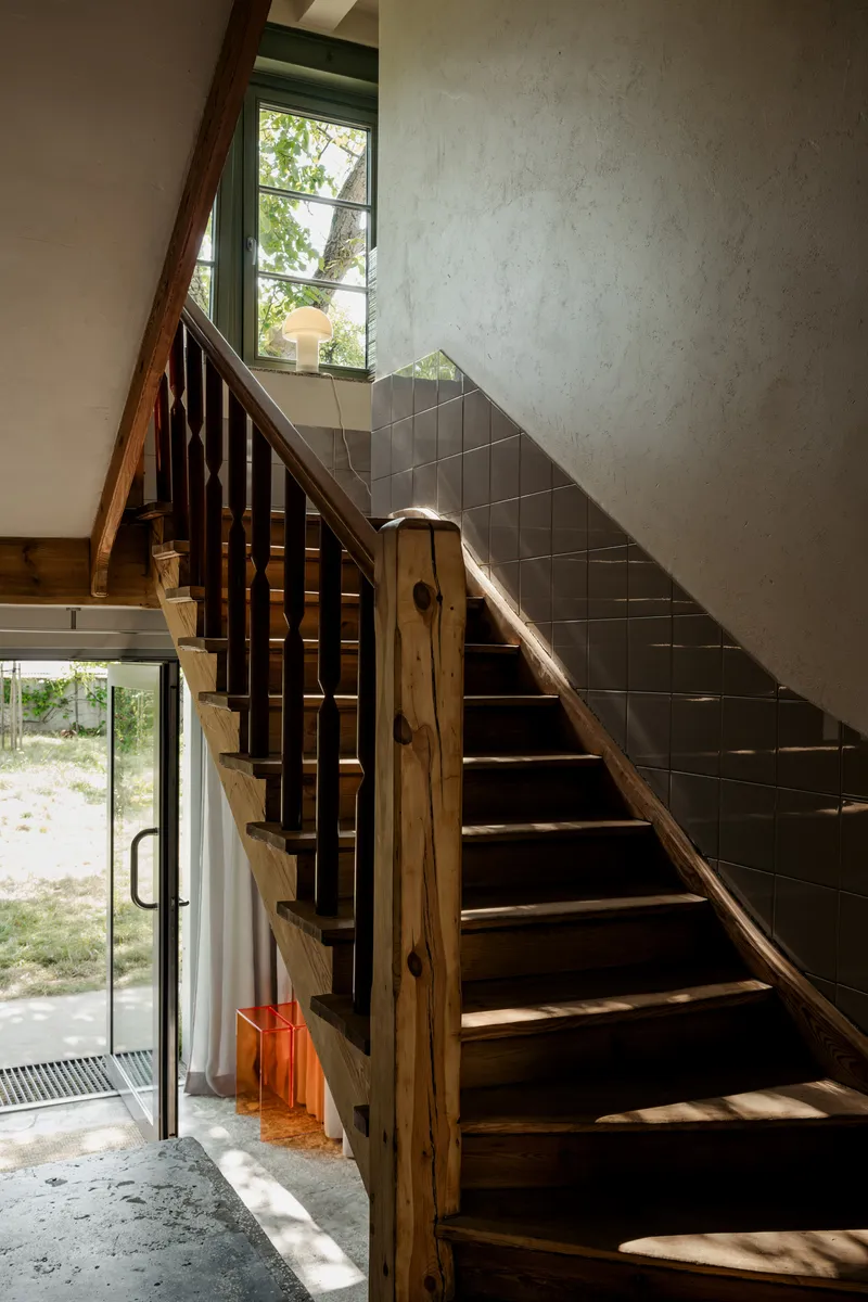 Timber staircase with dark painted treads and olive tile wainscoting in afternoon sunlight