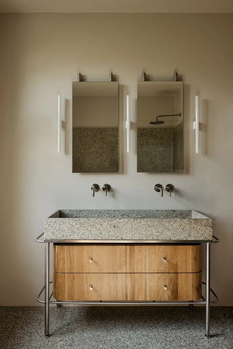 Double vanity with terrazzo sink on tubular steel frame below wall-mounted mirrors and sconces