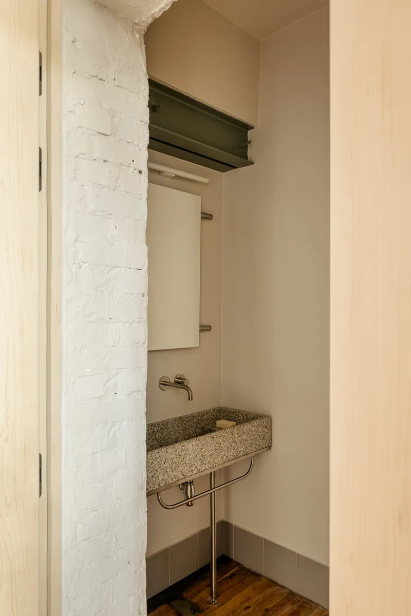 Compact powder room with terrazzo basin on metal stand beside painted brick wall
