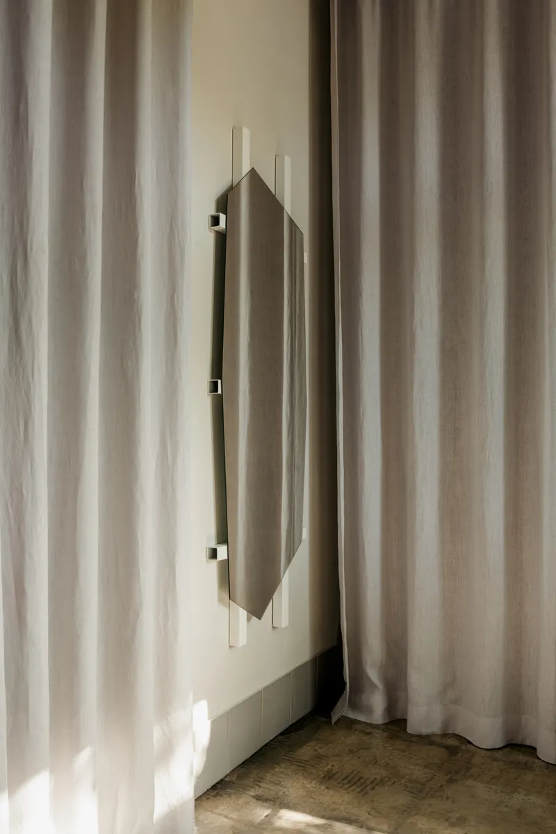 Vertical door pull on pale wall framed by sheer curtains in soft daylight