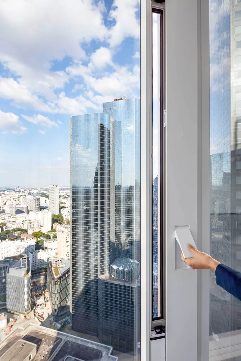 Interior window frame with hand holding tablet overlooking the neighboring glass tower and cityscape beyond