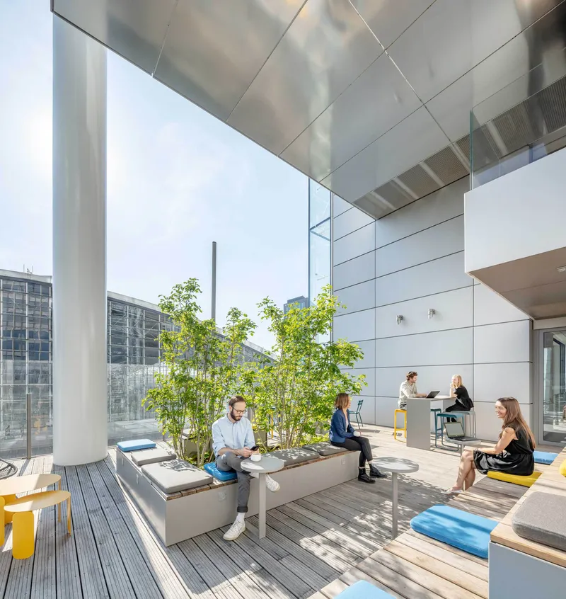 Rooftop terrace with timber decking, planted steel planter boxes and people seated under a suspended metal soffit