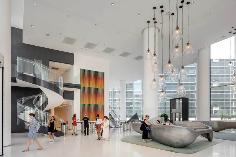 Double-height lobby with clustered glass pendant lights, a sculptural reception desk and visitors crossing the polished floor
