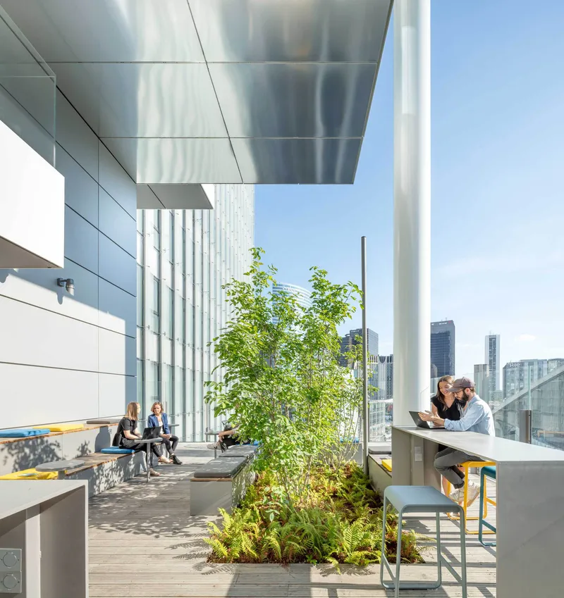 Outdoor terrace with aluminum ceiling panels, planted beds, timber decking and people working at tables