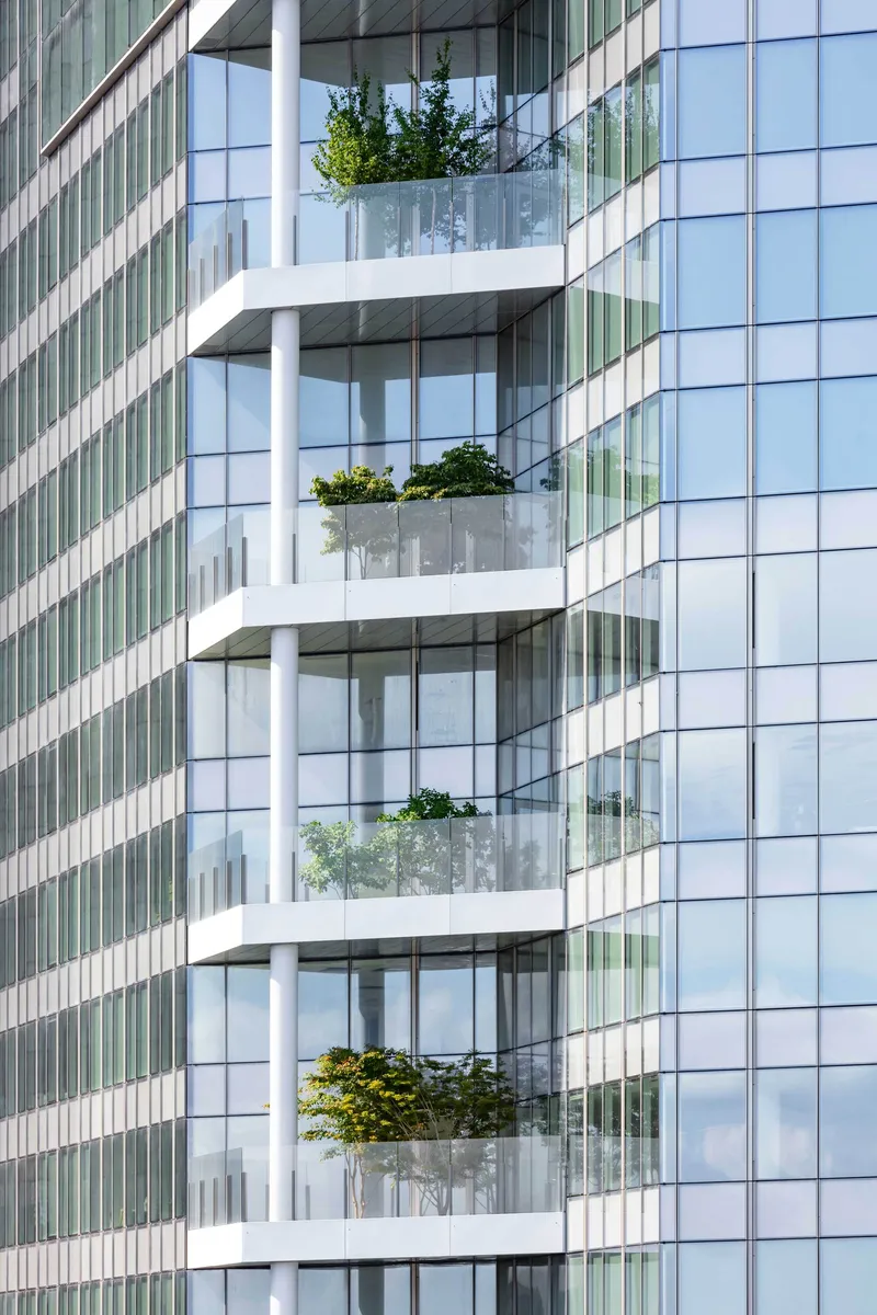 Stacked white balconies with planted beds projecting from the glass and metal panel facade