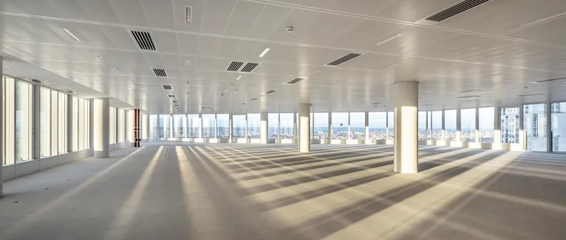 Empty office floor with concrete slab and cylindrical columns framed by floor-to-ceiling windows