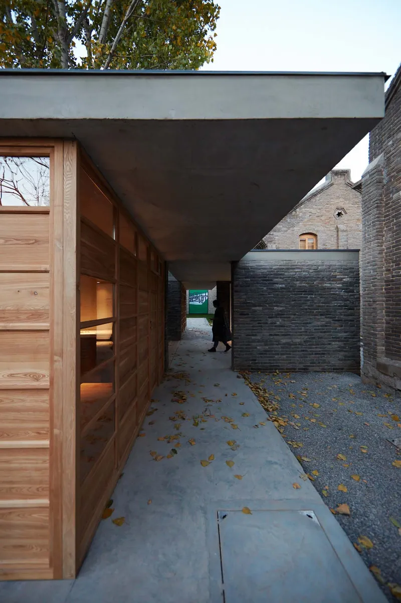 Covered entry passage with timber sliding doors and concrete soffit between brick walls scattered with autumn leaves