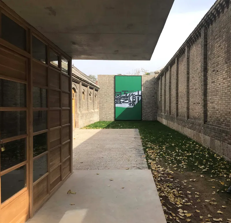 Concrete canopy sheltering a passage with timber screen and green painted door with graphic at the end