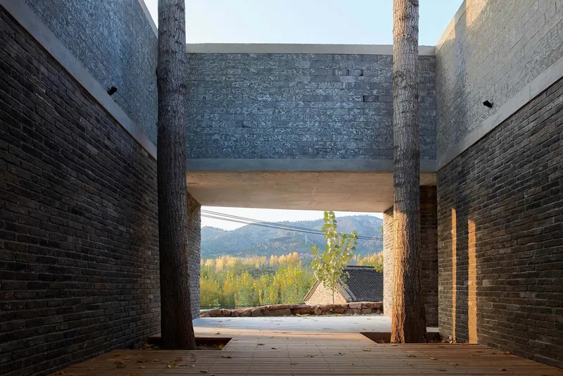 Framed view through brick passage with tree trunks capturing distant hills and golden autumn foliage at sunset