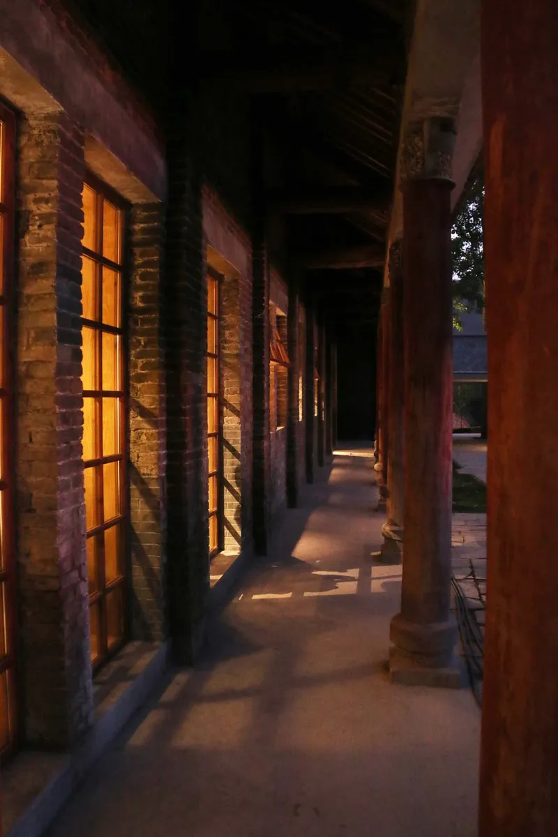 Covered exterior corridor with exposed brick columns and timber roof beams at dusk