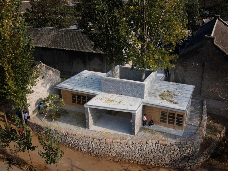 Aerial view of the interconnected volumes with gabion wall perimeter and courtyard between existing brick buildings