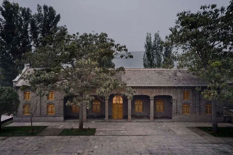 Restored brick facade with arched openings and tiled roof illuminated at dusk beneath overhanging trees