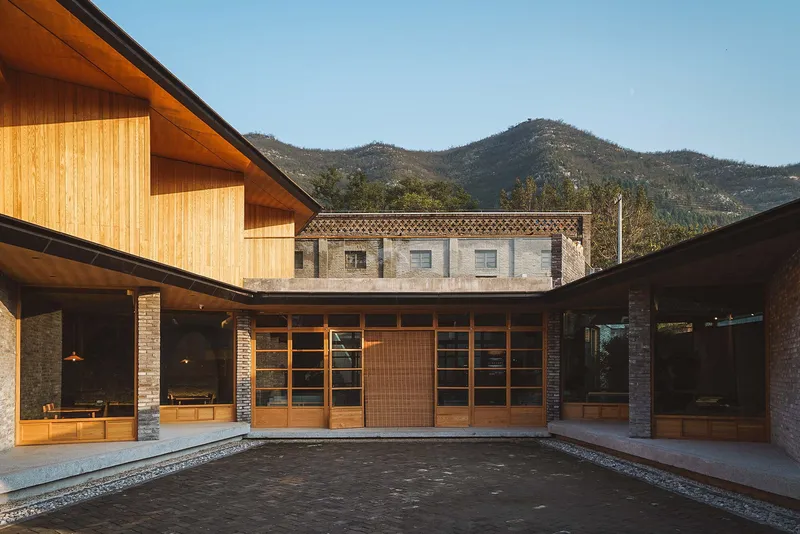 Courtyard view of timber-clad volumes with sloped roofs and stone base against distant mountains