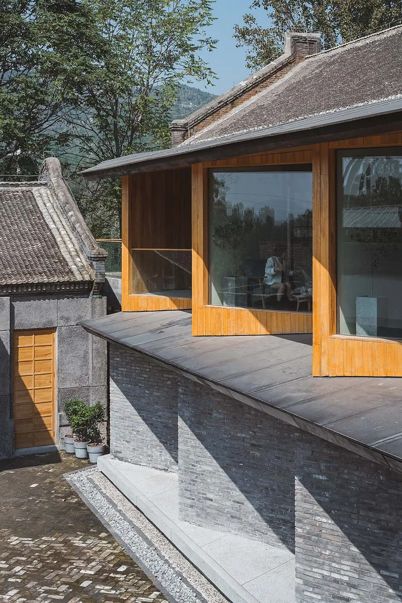 Timber-framed glazed addition with roof deck cantilevered over grey brick wall in afternoon light