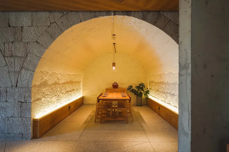 Vaulted stone dining room with uplighting and timber benches flanking a central table