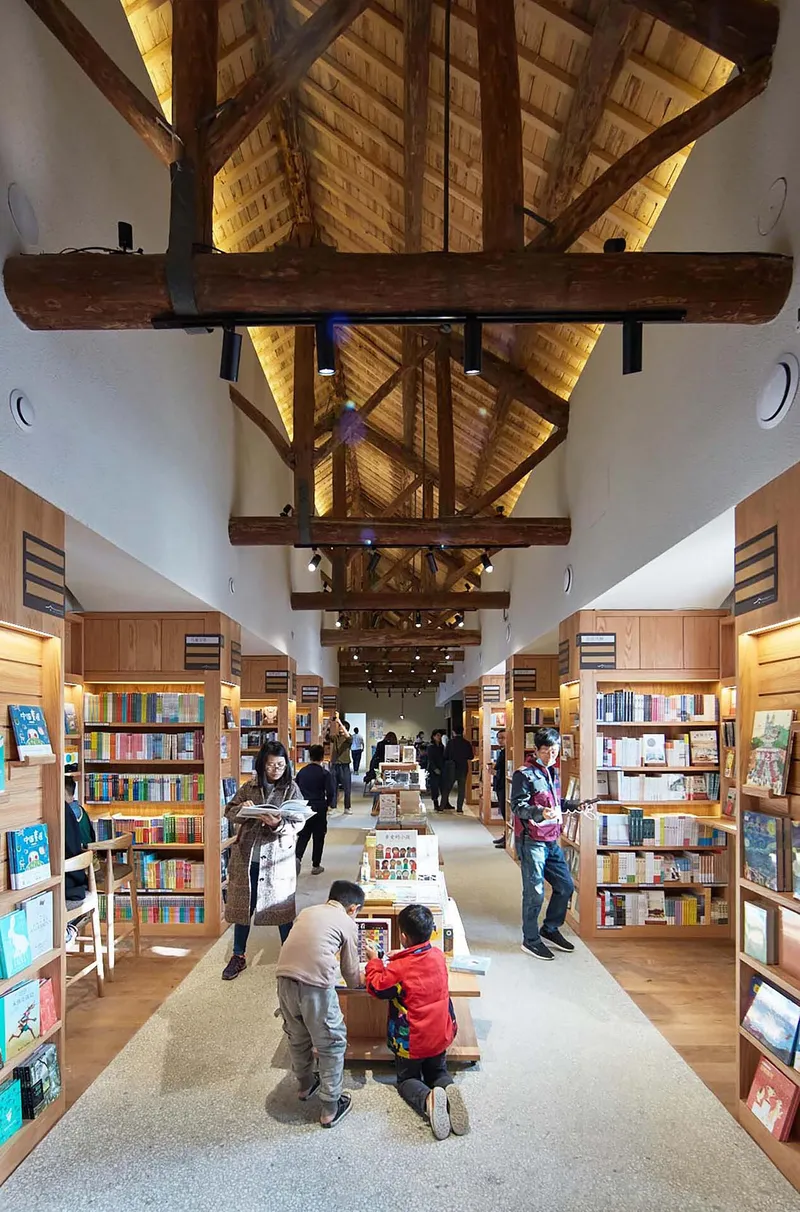 Interior view of a bookshop with exposed timber trusses and visitors browsing between wooden display shelves