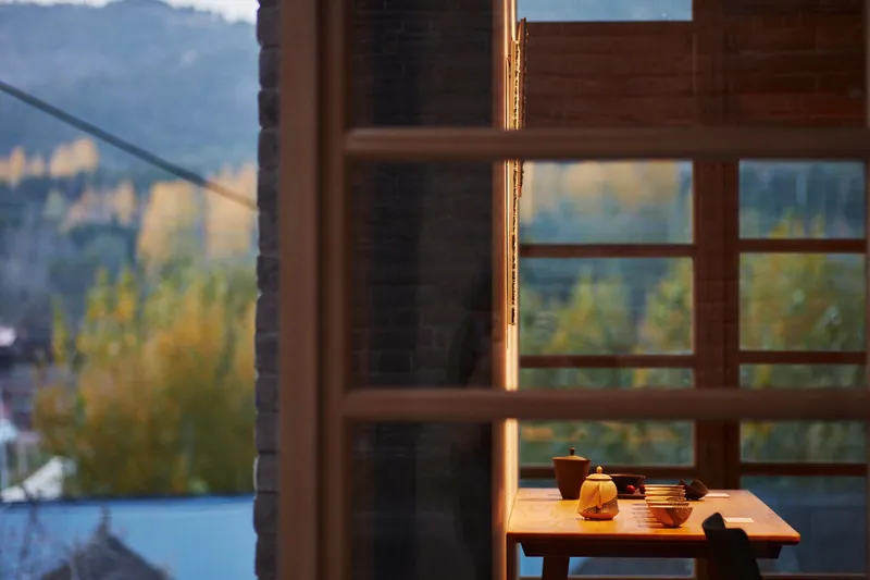 Low table with ceramic teaware beside gridded timber window at golden hour