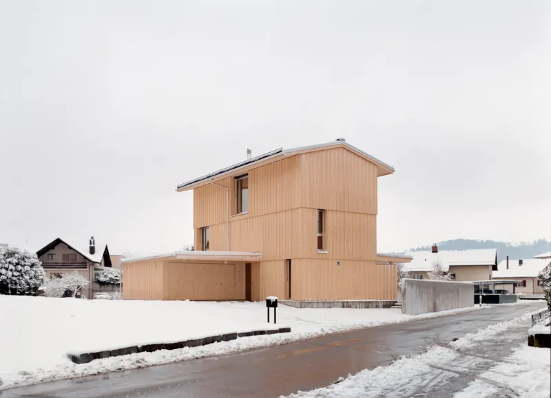 Street facade showing the stacked timber-clad volumes with glazed openings under an overcast winter sky