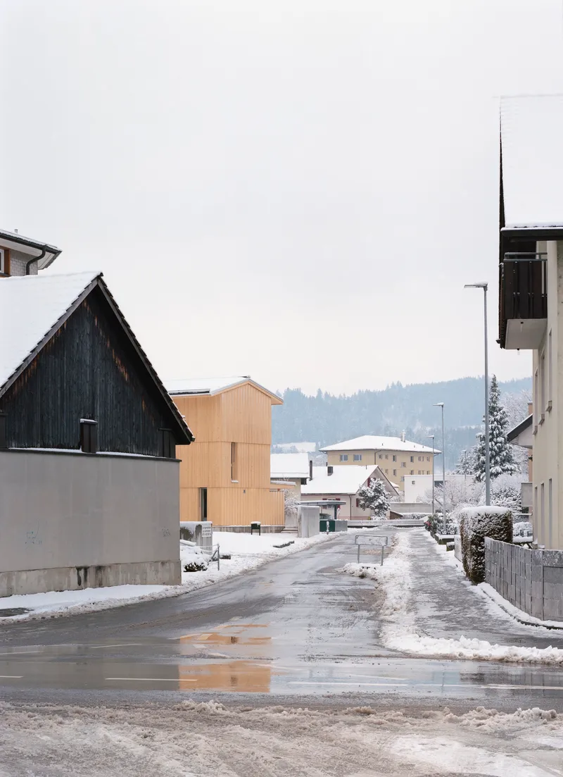 Timber house seen from a residential street intersection in winter with surrounding traditional buildings and forested hills