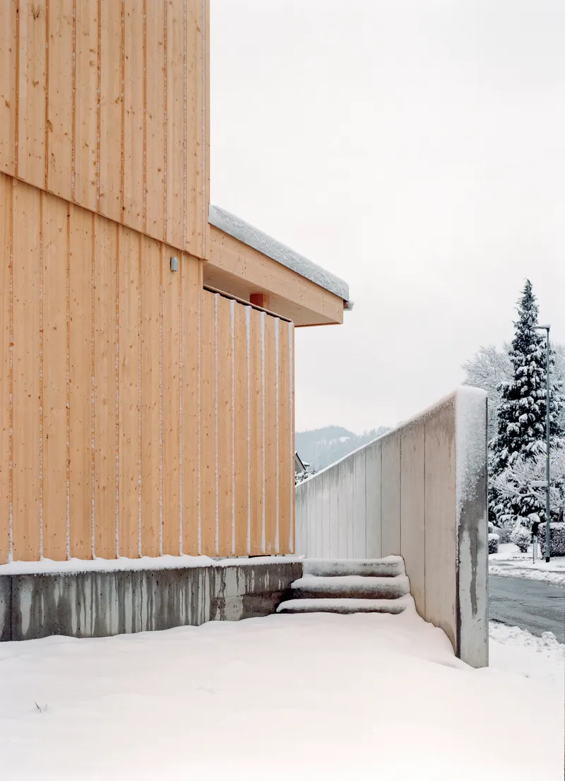 Vertical timber facade meeting concrete steps and wall covered in fresh snow