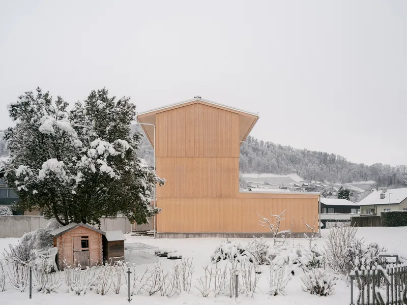 Rear view of the vertical timber-clad volume rising above a snow-covered garden with a small shed